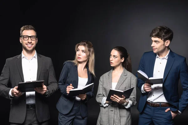 Group of business people looking at their smiling colleague with clipboard isolated on black — Stock Photo
