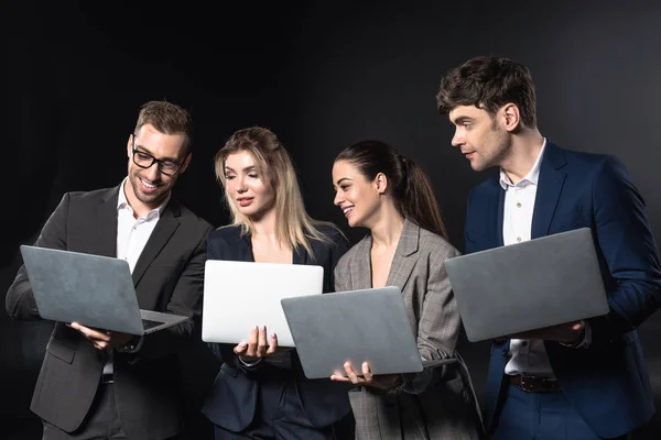 Group of happy business people working with laptops together isolated on black — Stock Photo