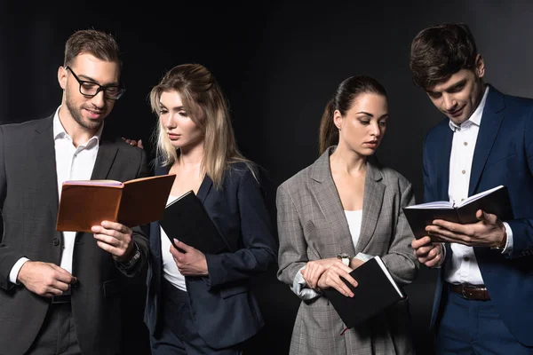 Group of serious business people reading notebooks together isolated on black — Stock Photo