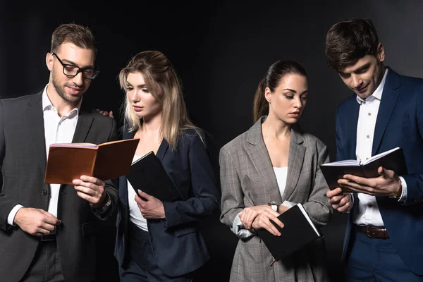 Gruppe seriöser Geschäftsleute liest gemeinsam Notizbücher isoliert auf schwarz — Stockfoto