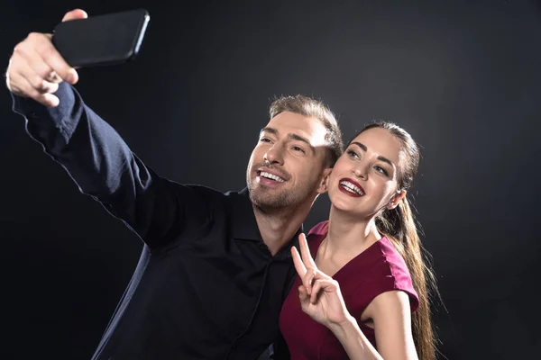 Feliz joven pareja tomando selfie con teléfono inteligente aislado en negro - foto de stock