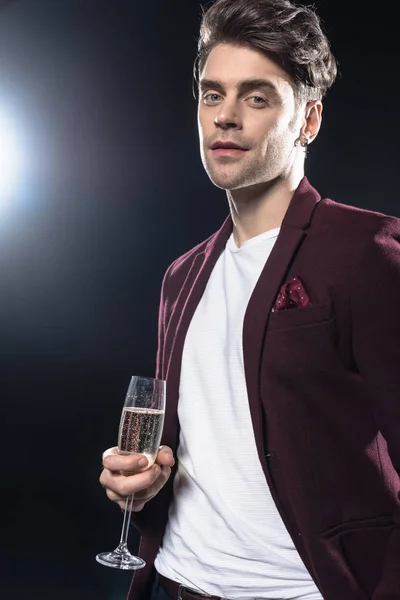 Attractive young man in stylish blazer holding champagne glass and looking at camera on black — Stock Photo