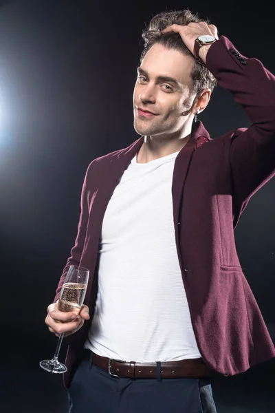 Schöner junger Mann in stylischem Blazer mit Champagnerglas und Blick in die Kamera auf schwarz — Stockfoto