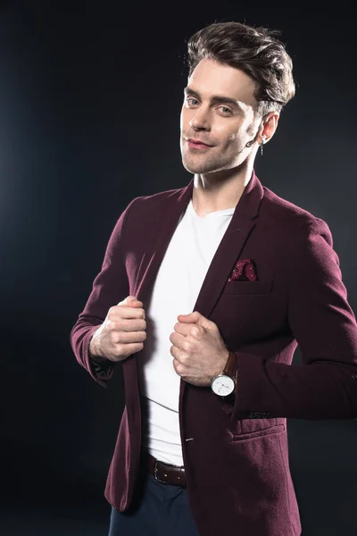 Attractive young man in stylish blazer looking at camera isolated on black — Stock Photo