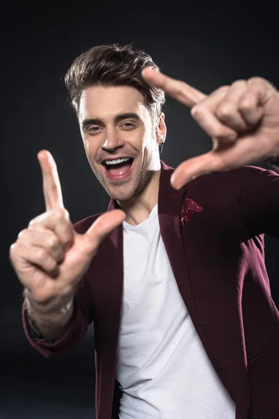 Close-up shot of happy young man showing frame gesture isolated on black — Stock Photo
