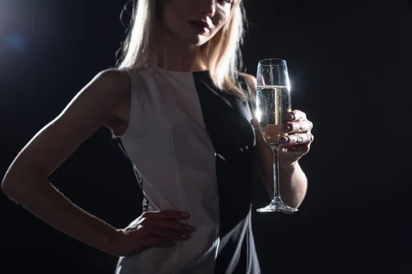 Tiro recortado de mujer joven sosteniendo una copa de champán en negro - foto de stock