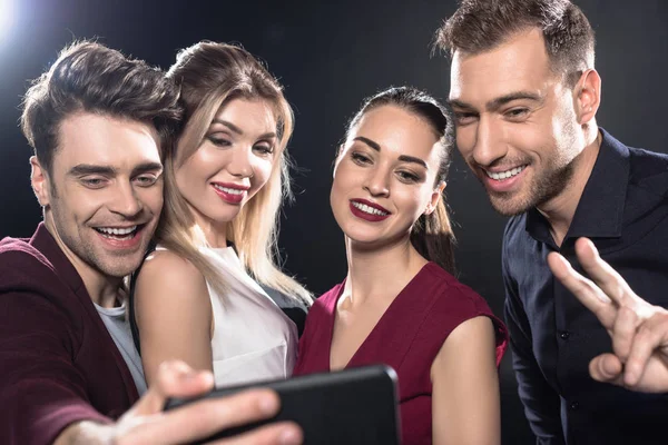 Primer plano de feliz grupo de amigos tomando selfie con teléfono inteligente durante la fiesta en negro - foto de stock