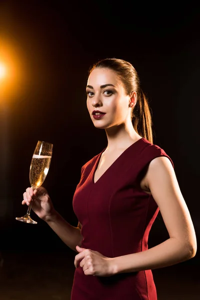 Beautiful young woman holding glass of champagne on black — Stock Photo