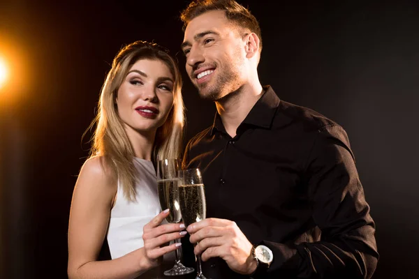 Happy young couple with glasses of champagne standing together on black — Stock Photo