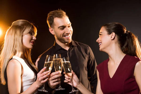 Grupo de amigos felices tintineo copas de champán bajo luz dorada en negro - foto de stock