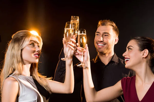 Group of smiling friends clinking champagne glasses under golden light on black — Stock Photo