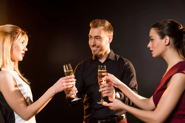 Smiling man giving champagne glasses to women during party on black — Stock Photo