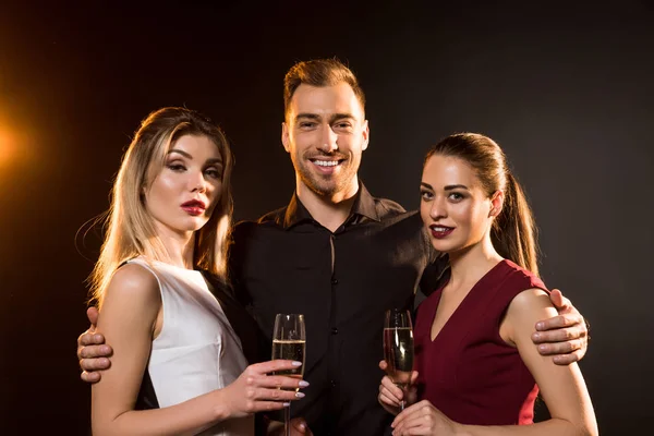 Smiling man and women holding champagne glasses and looking at camera on black — Stock Photo