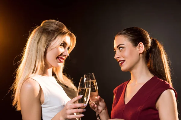 Beautiful young women in dresses clinking champagne glasses on black during new year party — Stock Photo