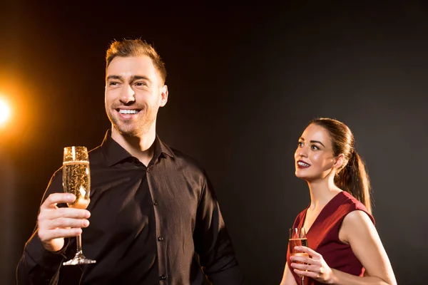 Happy young couple with glasses of champagne standing on black — Stock Photo