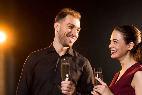 Feliz joven pareja con copas de champán coqueteando en negro - foto de stock