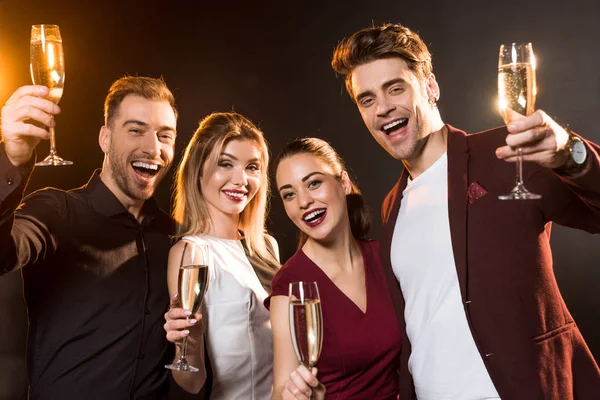 Група друзів тримає келихи шампанського і дивиться на камеру під час вечірки на чорному — стокове фото