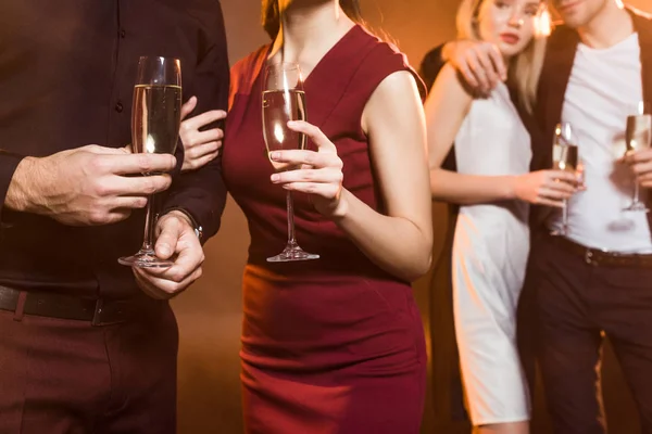 Tiro recortado de casais com copos de champanhe de pé sob luz dourada durante a festa — Fotografia de Stock