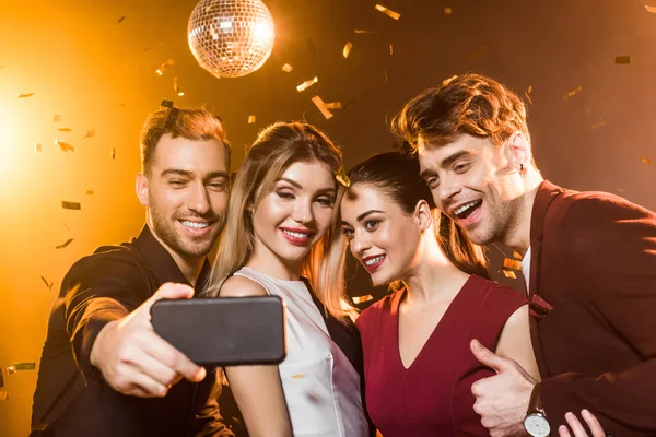 Группа улыбающихся друзей, делающих селфи со смартфоном во время вечеринки — стоковое фото