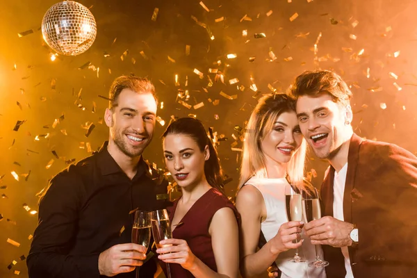 Grupo sonriente de amigos sosteniendo copas de champán y mirando a la cámara durante la fiesta - foto de stock