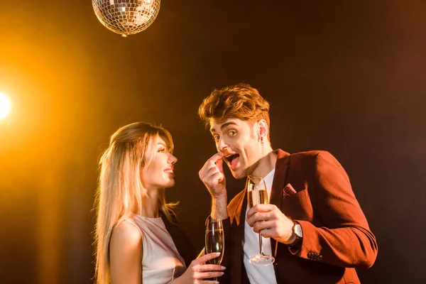 Feliz jovem casal com champanhe se divertindo durante a festa sob luz dourada — Fotografia de Stock