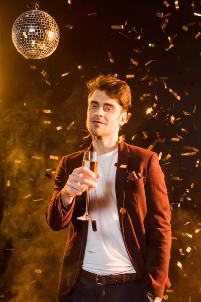 Handsome young man with champagne celebrating christmas with falling confetti — Stock Photo