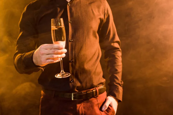 Tiro recortado de hombre con copa de champán bajo luz amarilla sobre negro - foto de stock