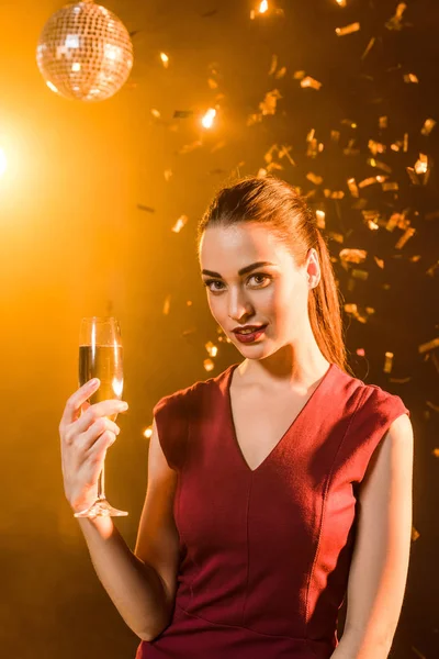 Attractive young woman with champagne glass under falling confetti, christmas concept — Stock Photo