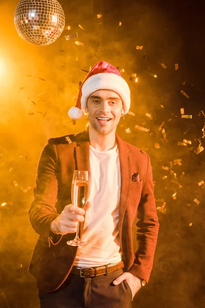 Jovem sorridente com champanhe celebrando o Natal com confetes caindo — Fotografia de Stock