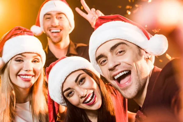 Gros plan du groupe d'amis dans chapeaux Santa célébrer le nouvel an et regarder la caméra — Photo de stock