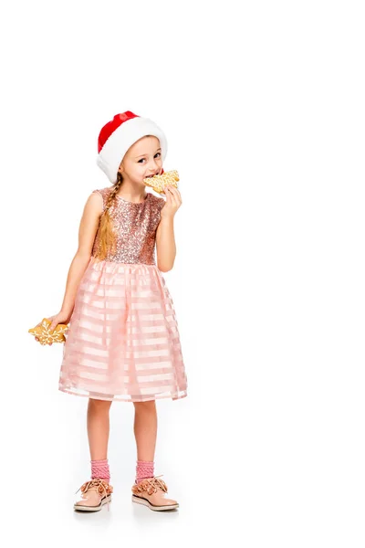 Entzückendes kleines Kind mit Weihnachtsmann, das Ingwerkekse isst und isoliert auf weiß in die Kamera schaut — Stockfoto