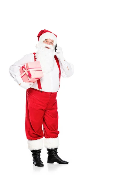 Père Noël claus dans les bretelles tenant boîte cadeau et parler par téléphone isolé sur blanc — Photo de stock