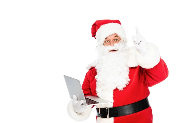 Santa claus holding laptop and looking at camera while pointing up isolated on white — Stock Photo