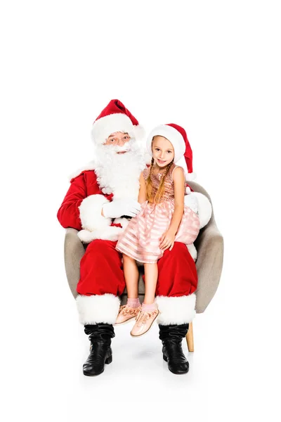 Père Noël Claude et petit enfant assis dans le fauteuil ensemble et regardant la caméra isolée sur blanc — Photo de stock