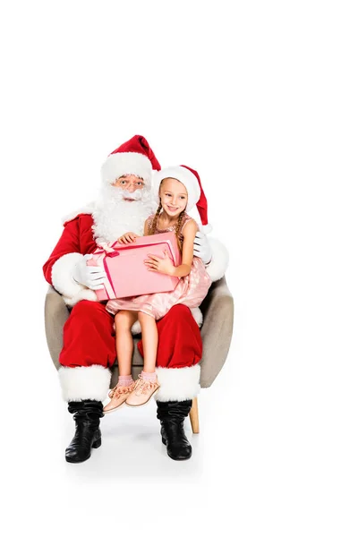 Père Noël Claude et petit enfant assis dans un fauteuil ensemble et tenant boîte cadeau isolé sur blanc — Photo de stock