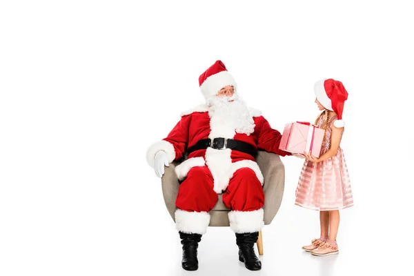Санта Клаус сидит в кресле и дарит подарок маленькому ребенку, изолированному на белом — стоковое фото