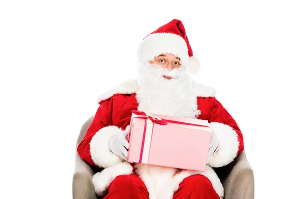 Santa claus sentado en sillón con caja de regalo y mirando a la cámara aislada en blanco - foto de stock