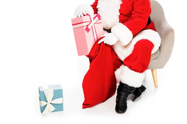 Обрізаний знімок Санти Клауса сидить у кріслі з подарунками та сумкою ізольовано на білому — стокове фото