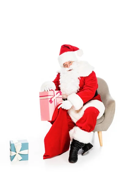 Santa claus sitting in armchair with various presents isolated on white — Stock Photo