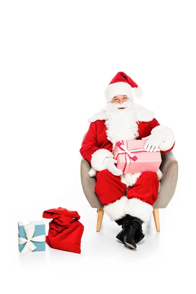 Santa claus sitting in armchair with various gift boxes isolated on white — Stock Photo