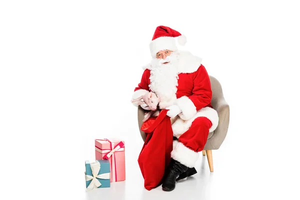 Santa claus con regalos sentado en sillón con cerdito aislado en blanco - foto de stock