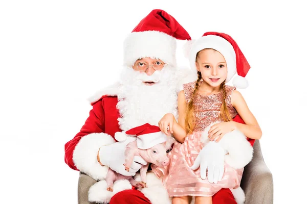 Santa claus e feliz criança sentada em poltrona com porquinho e olhando para a câmera isolada no branco — Fotografia de Stock