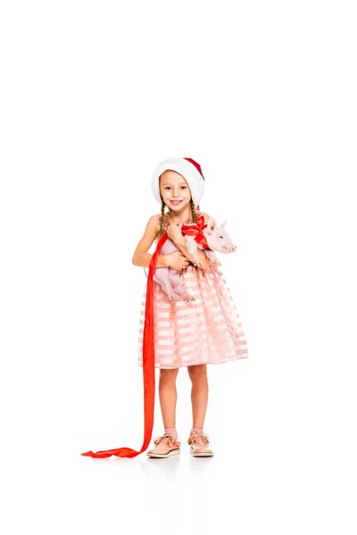 Adorable little child in santa hat holding piggy and looking at camera isolated on white — Stock Photo