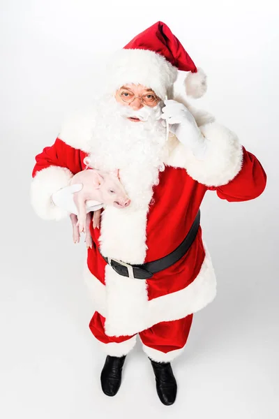 Hochwinkelige Ansicht des Weihnachtsmannes, der Schwein hält und mit dem Smartphone spricht, isoliert auf weiß — Stockfoto