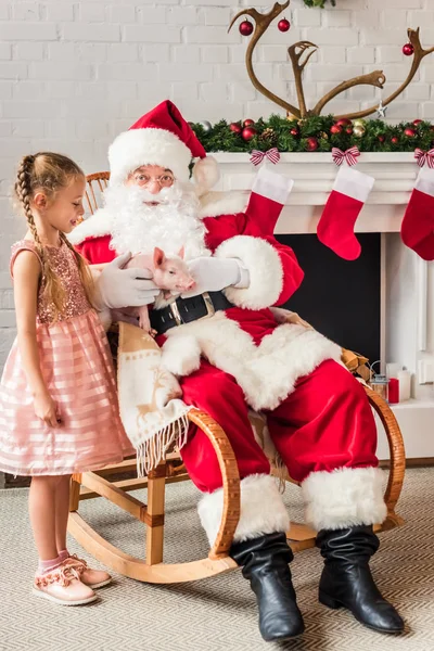 Santa claus and cute little child playing with adorable pig at christmas eve — Stock Photo