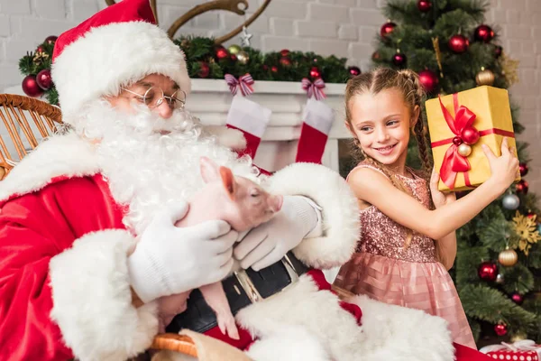 Santa brincando com porco e bonito sorrindo criança segurando caixa de presente — Fotografia de Stock