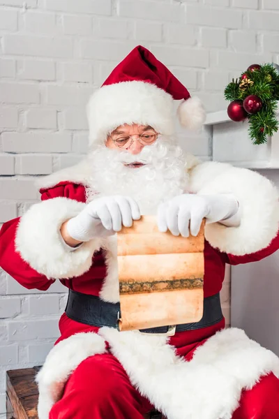 Père Noël claus assis sur la poitrine et tenant parchemin avec wishlist — Photo de stock