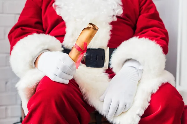 Close-up partial view of santa claus holding rolled parchment with wishlist — Stock Photo