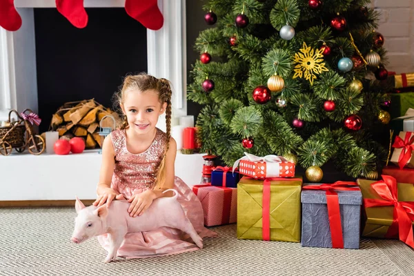 Adorable little child playing with pig and smiling at camera at christmas time — Stock Photo