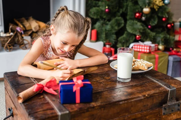 Lindo niño sonriente escribiendo lista de deseos en pergamino en Navidad - foto de stock